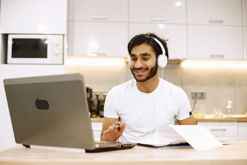Muslim man learning Quran pronunciation online with laptop and headphones.