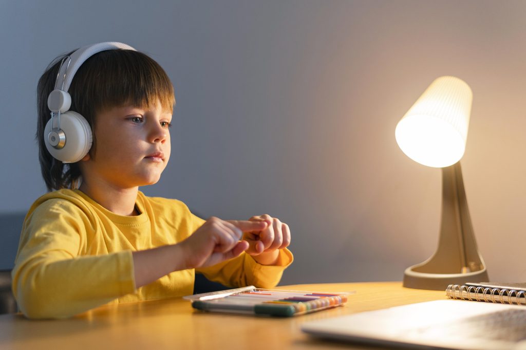 A young boy learning the Quran online from home with headphones and a laptop.